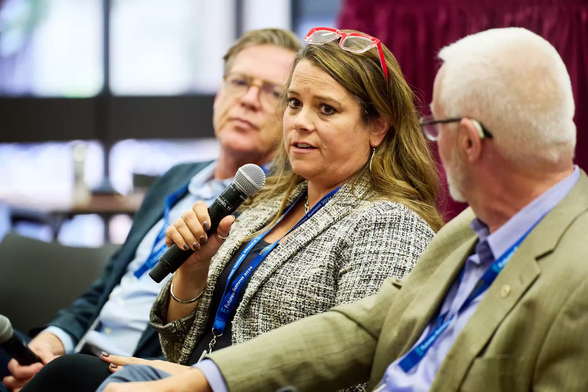 A woman in a chair addresses an audience, speaking into a microphone with clarity and engagement.