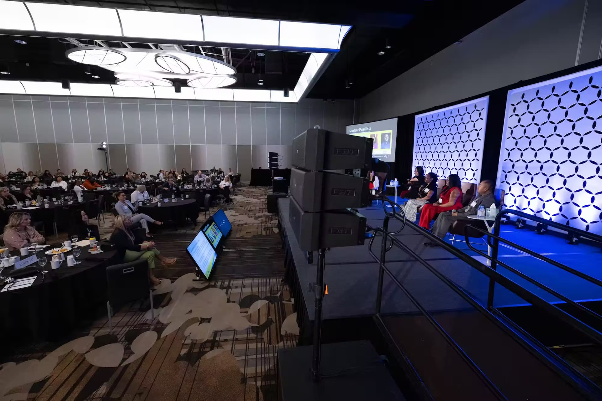 A spacious room filled with seated individuals facing a stage, creating an atmosphere of engagement and anticipation.