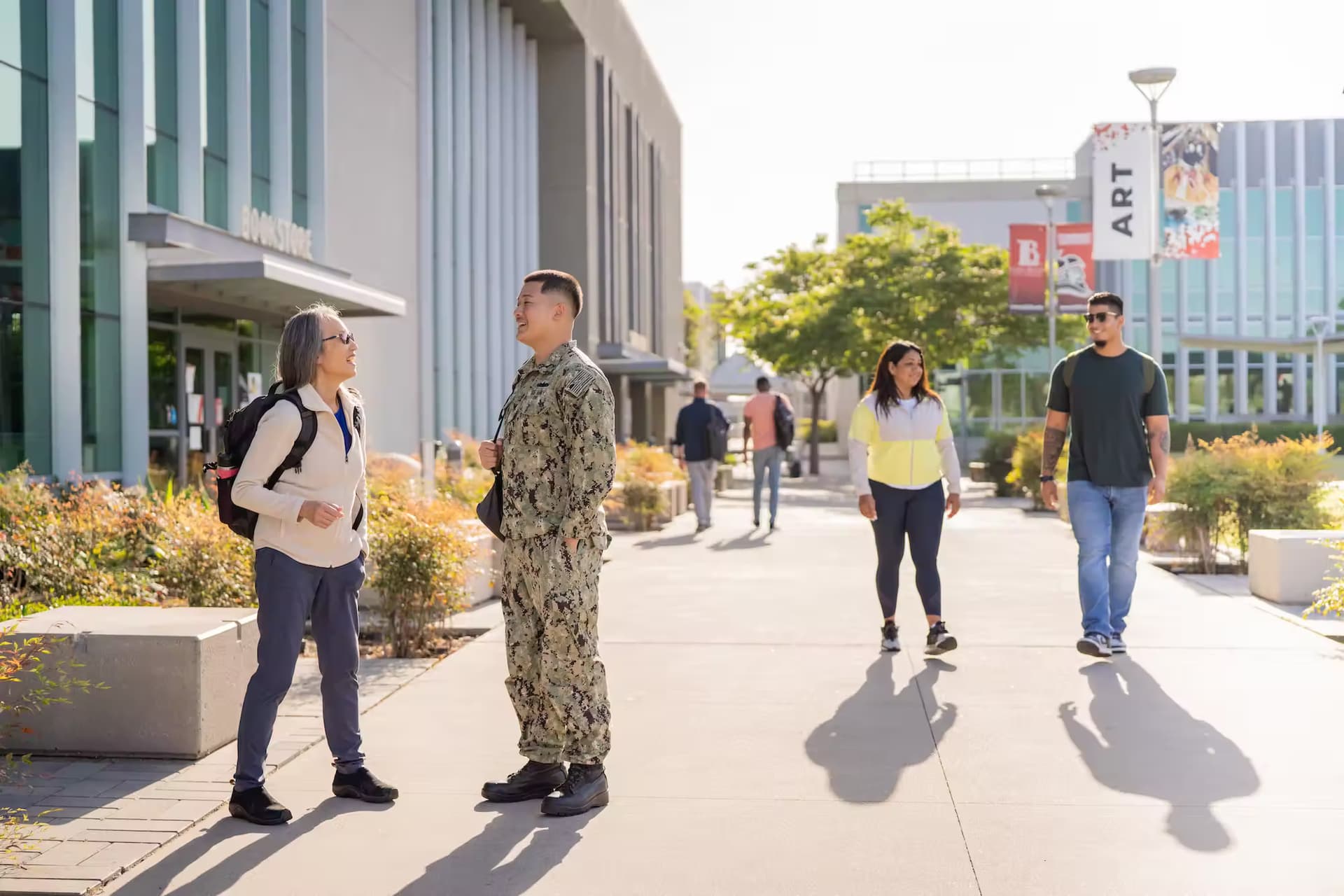 Four students, one in military uniform, outside a bookstore in a college campus