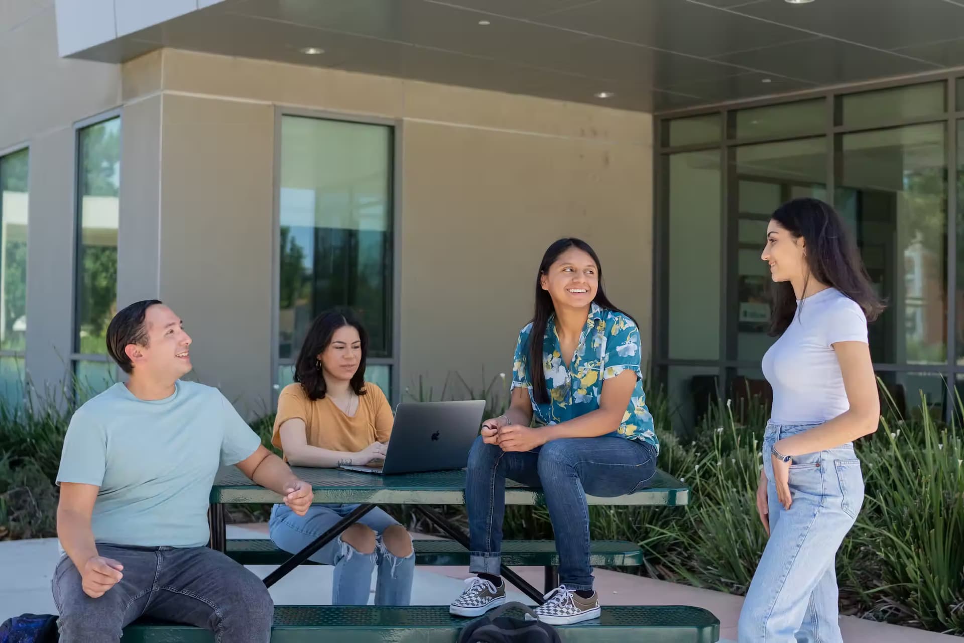 Four students talking on a picnic table outside a college building